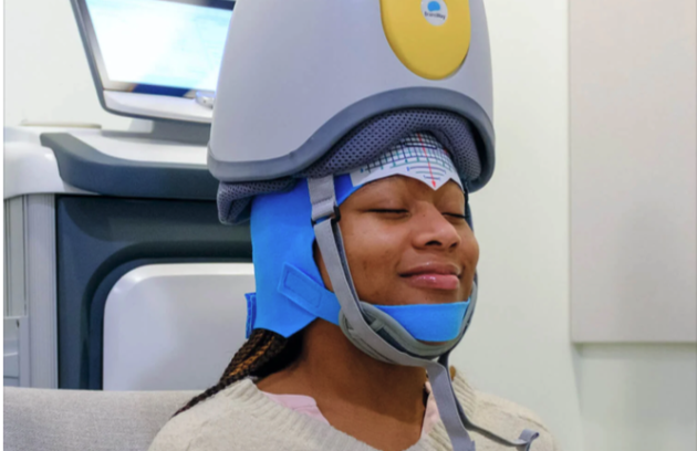 A woman wearing a headpiece of TMS therapy and looking ecstatic